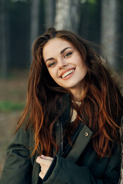 улыбающаяся женщина в куртке на открытом воздухе в лесном путешествии - Фото, изображение