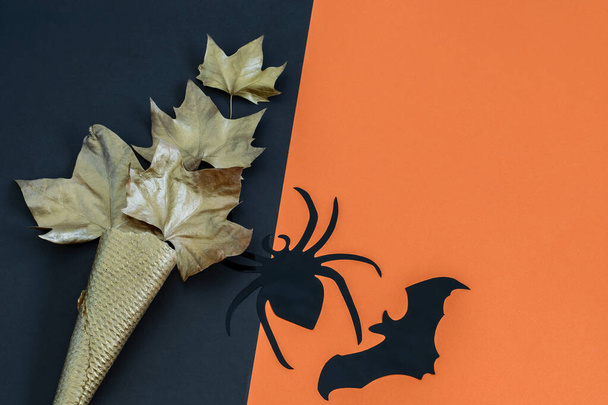Halloween tło z pająkiem, nietoperzem i złotym stożkiem lodów gofrowych ze złotymi liśćmi na czarno-pomarańczowym tle. Zaproszenie na imprezę, kartka okolicznościowa z miejscem do kopiowania.  - Zdjęcie, obraz