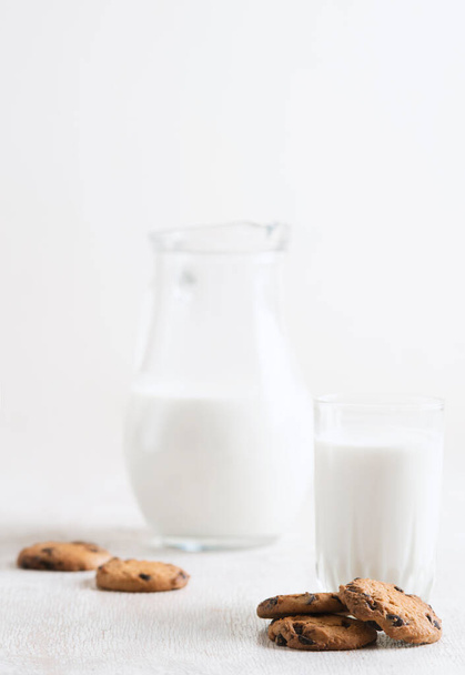 chocolate chip cookies and milk in a jug and a glass on a white wooden  background - Fotoğraf, Görsel