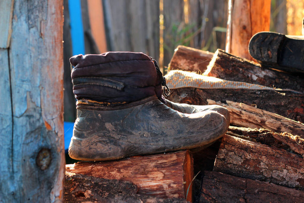 Stare gumowe buty na stercie drewna opałowego, koncepcja wiejskiego stylu życia - Zdjęcie, obraz