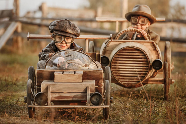 Two boys, riders compete against each other on homemade wooden car on rural road. Retouch for retro - Fotó, kép