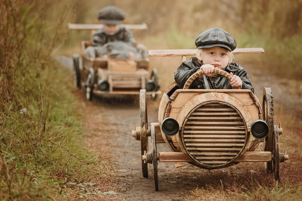 Two boys, riders compete against each other on homemade wooden car on rural road. Retouch for retro - Foto, immagini