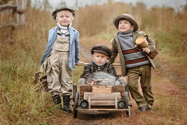 Three little boys racers compete in improvised wooden cars on the background of the rural landscape autumn rainy day. Retouch for retro - Foto, immagini