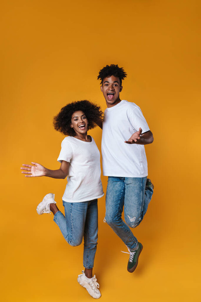 Image of delighted african american couple laughing while jumping isolated over yellow wall - Fotoğraf, Görsel
