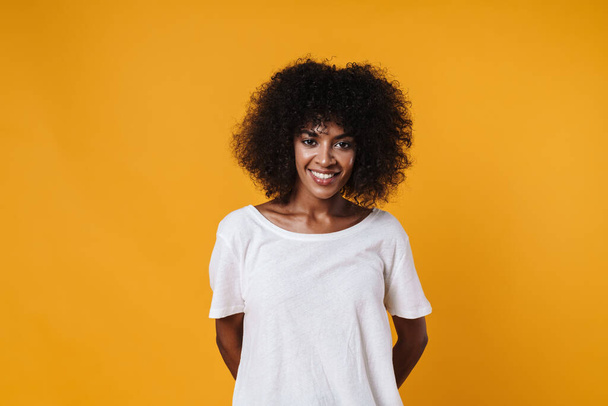 Image of happy african american girl smiling and looking at camera isolated over yellow wall - Фото, изображение