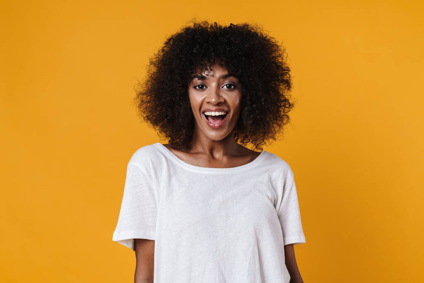 Image of excited african american girl smiling and looking at camera isolated over yellow wall - Фото, изображение