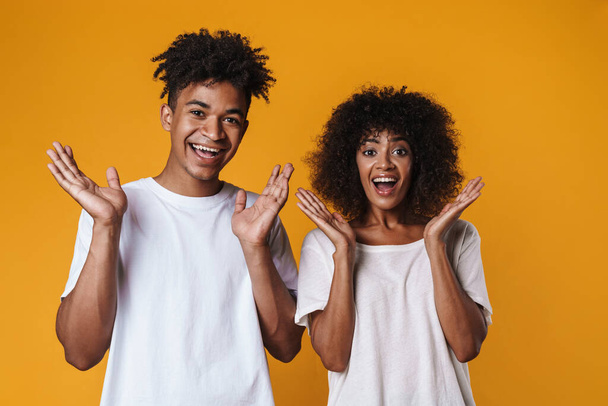 Image of excited african american couple posing with throwing up hands isolated over yellow wall - Fotoğraf, Görsel