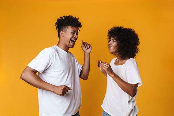 Image of cheerful african american couple dancing and singing isolated over yellow wall - Foto, immagini