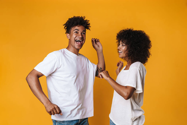 Image of cheerful african american couple dancing and singing isolated over yellow wall - Foto, afbeelding