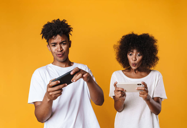 Photo of excited african american people playing online game on cellphones isolated over yellow background - Foto, afbeelding
