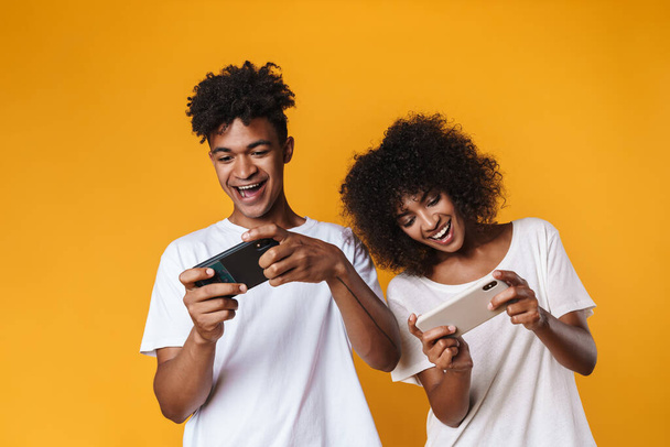 Image of cheerful african american couple playing online game on smartphones isolated over yellow wall - Foto, Bild