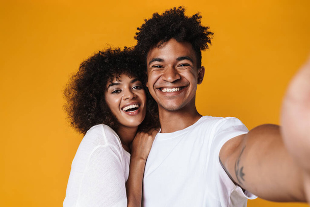 Image of african american couple hugging and smiling while taking selfie photo isolated over yellow wall - 写真・画像