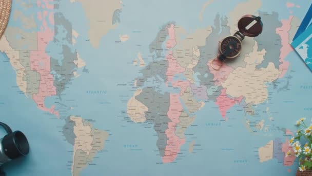 Zoom horizontal du dessus plan plat de la carte du monde avec des objets de voyage sur une table en bois - Séquence, vidéo