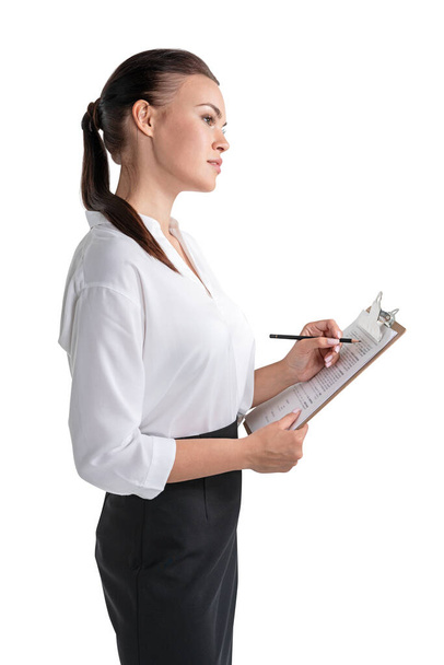 Isolated side portrait of serious young European businesswoman standing with clipboard over white background. - Zdjęcie, obraz