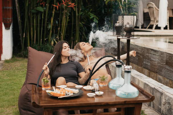 Group of young girls smoking a hookah and exhaling white smoke. Vacation. - Valokuva, kuva