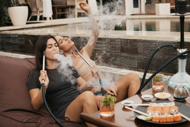 Group of young girls smoking a hookah and exhaling white smoke. Vacation. - Valokuva, kuva