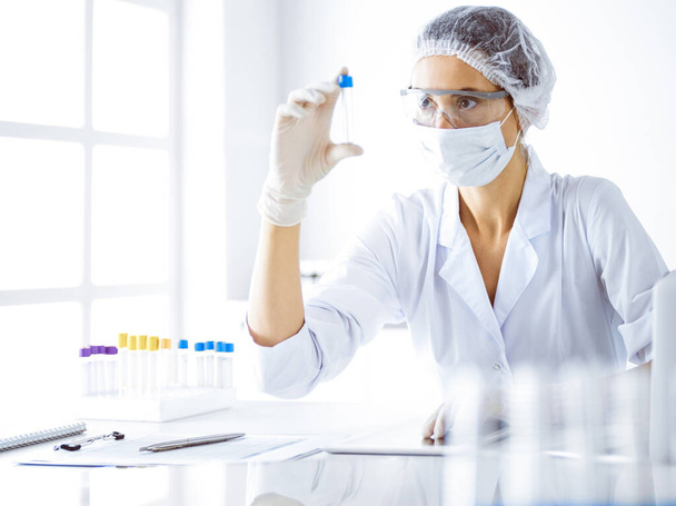 Professional female scientist in protective eyeglasses researching tube with reagents in laboratory. Concepts of medicine and science researching - Foto, Imagem