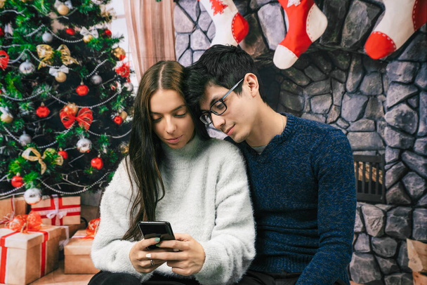 Para patrząc na telefon komórkowy z tle Bożego Narodzenia - Zdjęcie, obraz