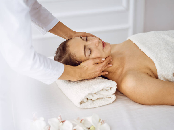 Beautiful brunette woman enjoying facial massage with closed eyes. Relaxing treatment in medicine and spa center concepts - Valokuva, kuva