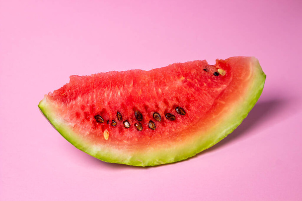 Watermeloen op een roze achtergrond. Snijd een stuk watermeloen af. Rode rijpe watermeloen - Foto, afbeelding