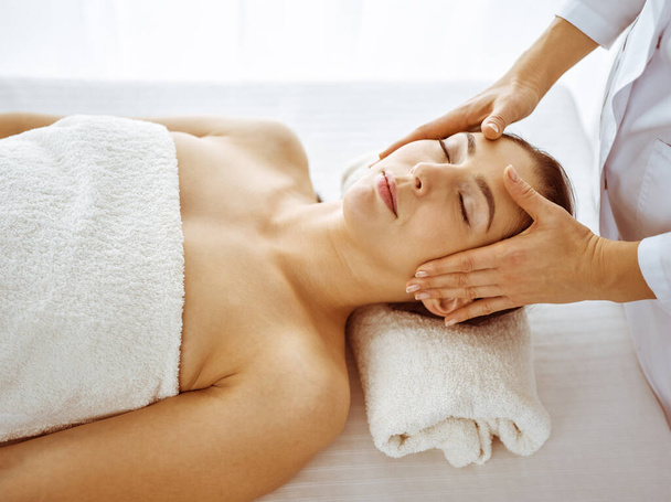 Beautiful brunette woman enjoying facial massage with closed eyes. Relaxing treatment in medicine and spa center concepts - Φωτογραφία, εικόνα