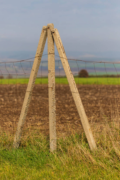 postes delgados de hormigón en el campo entre los que hay una valla tensada. El paisaje está en el fondo. - Foto, Imagen