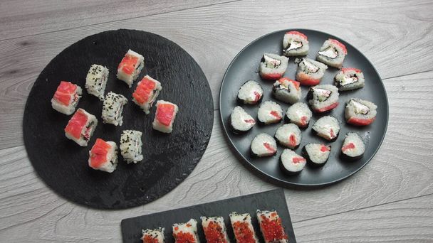 La mano femenina toma comida con palillos. Composición de comida japonesa. Varios tipos de sushi colocados en tablero de piedra negra. Ensalada de kimchi picante, sopa de wonton, palillos y salsa de soja. - Foto, imagen