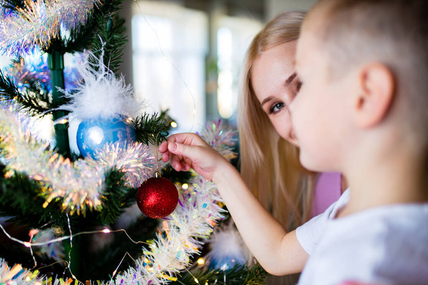 Child and mother decorating Christmas tree at home self-isolation in quarantine due to coronavirus - Foto, immagini