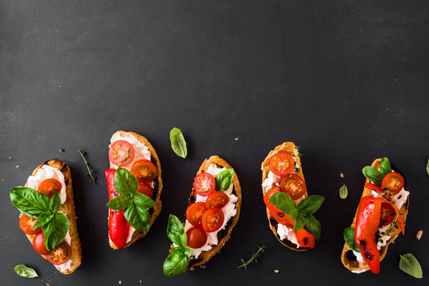 Bruschetta sandwiches with tomatoes, cream cheese, grilled paprika and basil on dark background, top view, copy space. Traditional italian snack - grilled bruschetta toasts. - Фото, изображение