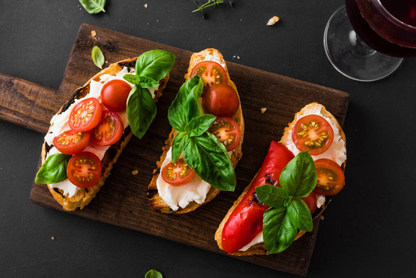 Bruschetta sandwiches with tomatoes, cream cheese, grilled paprika and basil on wooden board, close up. Traditional italian snack for wine - grilled bruschetta toasts. - Foto, imagen