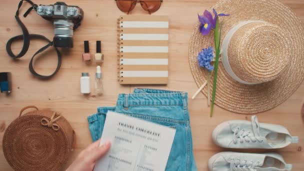 Conceptual top-view flat lay footage of unrecognizable female hands holding travel checklist packing suitcase and hand luggage - Filmagem, Vídeo