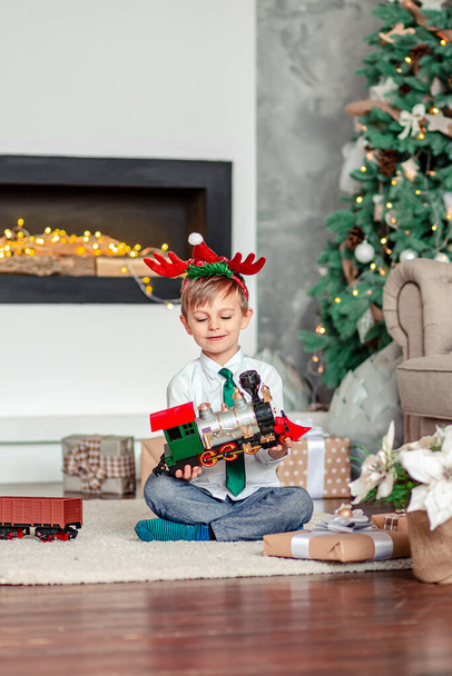 Good morning. Happy little boy with a gift, toy train, under the Christmas tree on a New Year's morning. A time of miracles and fulfillment of desires. Merry Christmas. - Фото, изображение