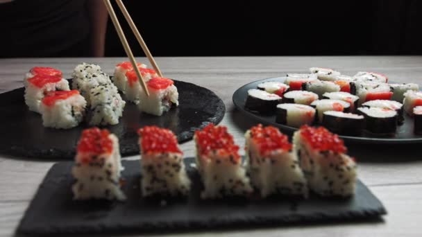 Joukko Sushi Rolls tonnikalaa, lohta, kurkkua, avokado ripottele seesaminsiemeniä mustalla taustalla lähikuva. Erilaisia japanilaisia ruokia ravintolassa. - Materiaali, video
