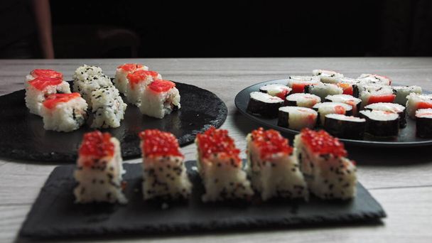 Sushi Rolls szett tonhallal, lazaccal, uborkával, avokádóval, szezámmaggal fekete háttér közeli felvételen. Japán ételek választéka az étteremben. - Fotó, kép