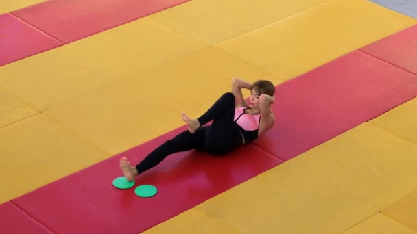 Una chica hermosa y delgada hace ejercicios con discos deslizantes en el gimnasio. - Metraje, vídeo