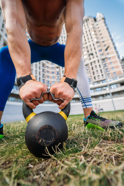 Sportive guy training with kettlebell on the background of a tall building. - Photo, Image