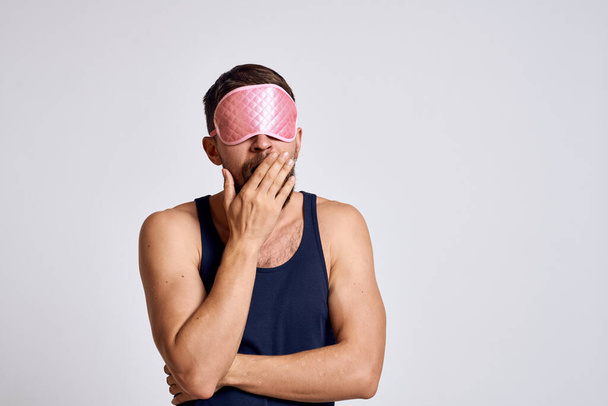 Un homme avec un masque de sommeil rose ET un T-shirt noir sur fond gris vue recadrée - Photo, image