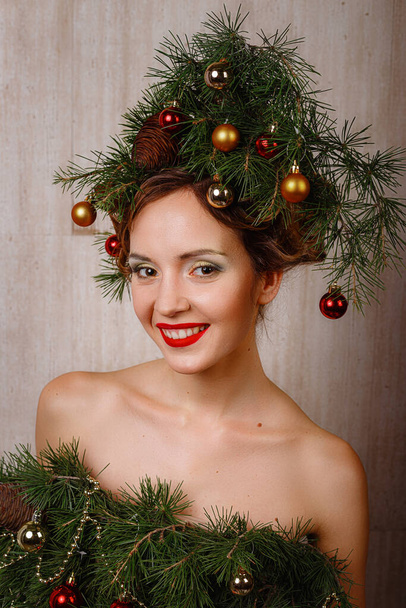 Beautiful happy young lady with a Christmas pine wreath on her head and fashione xmas tree dress, decorated with Christmas balls, berries and snowflakes. New Year Concept - Φωτογραφία, εικόνα