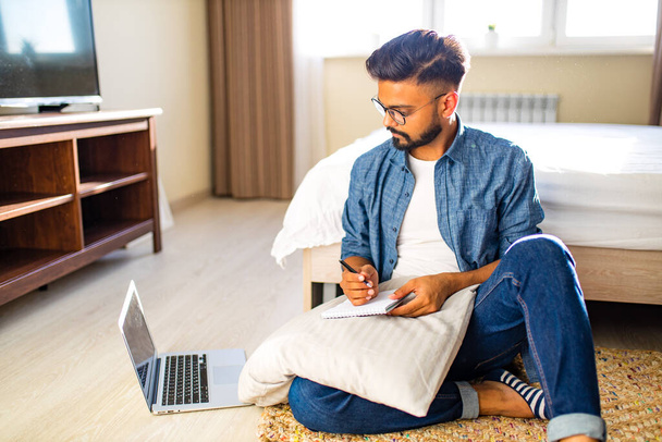 indian bearded male sitting on the floor and making making financial calculations online business in new apartment - Zdjęcie, obraz