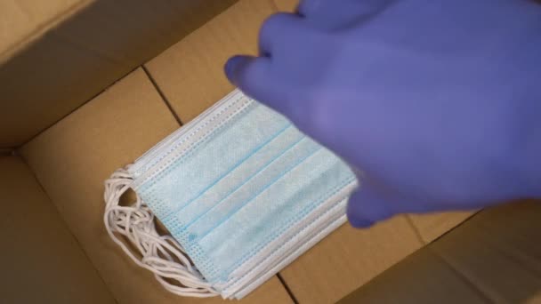 doctor in blue protective medical gloves picks up a pack of respirator masks from a brown cardboard delivery box. Coronavirus pandemic humanitarian aid and protection concept - Séquence, vidéo