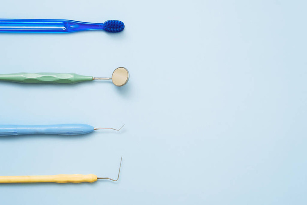 歯ブラシとミラー、ピンセットと青の背景に歯科治療のためのプローブ。平らなレイアウト、コピースペース - 写真・画像