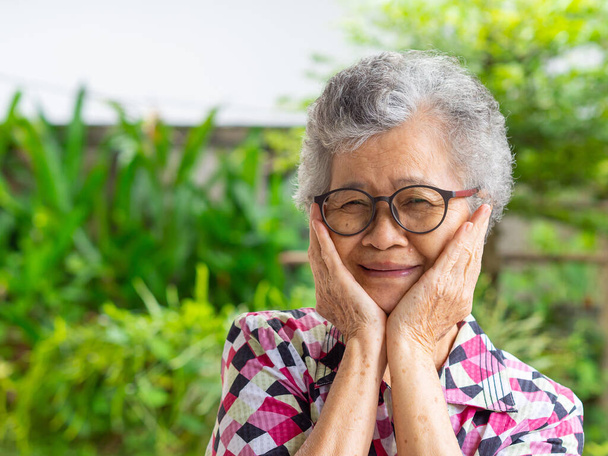 Зблизька усміхнена старша жінка і руки торкаються її обличчя. Азійська літня жінка здорова і має позитивні думки про життя, які роблять її щасливою щодня. - Фото, зображення