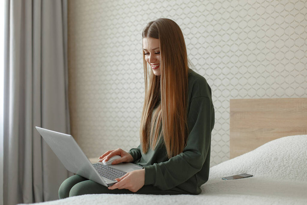Γυναίκα κάθεται σε ένα κρεβάτι και χρησιμοποιεί ένα φορητό υπολογιστή - Φωτογραφία, εικόνα