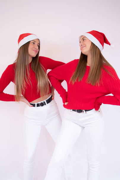 Portrait of two pretty young teenage girls wearing santa hat standing isolated over white background - Photo, Image
