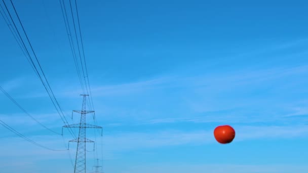 Een oranje veiligheidshelm vliegt de lucht in tegen een blauwe lucht en hoogspanningsdraden.  - Video