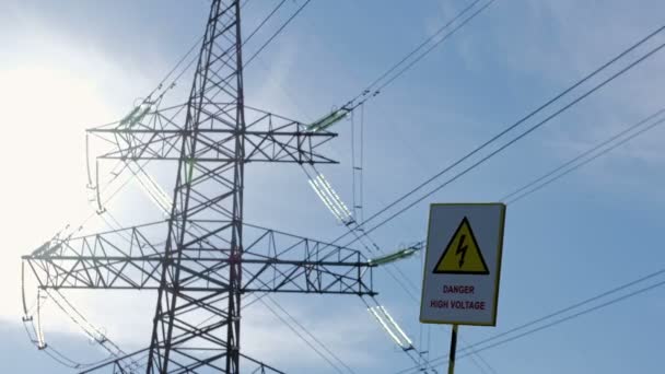 The "Caution High Voltage" sign sways against the backdrop of a metal pole of a high-voltage power line in the back sun. - Footage, Video