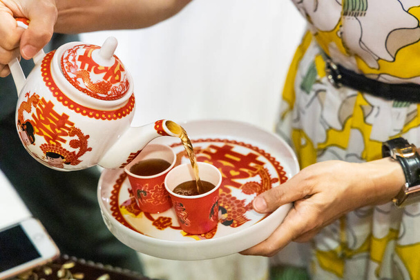 Persona llenando dos tazas desechables con té en la ceremonia de boda china. Palabra china en bandeja, olla y taza se traduce como Celebración en Inglés. - Foto, imagen