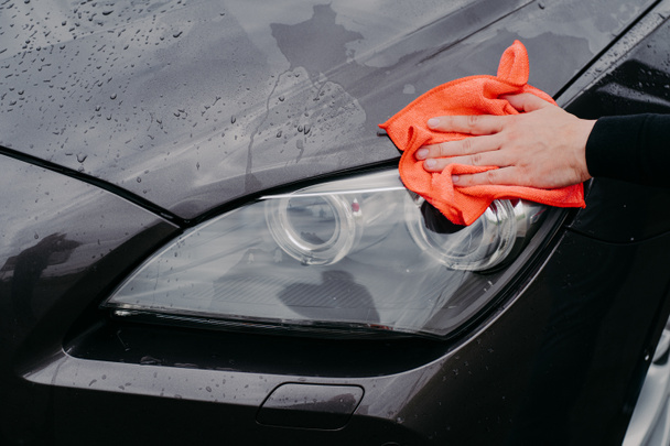 ラグ車のヘッドランプを拭くと男の手。洗車場での濡れた黒い自動車の清掃自動車の清掃とサービスのコンセプト - 写真・画像