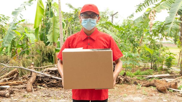 Asijské mladý muž dodávky v červené uniformě s balíčky - Fotografie, Obrázek