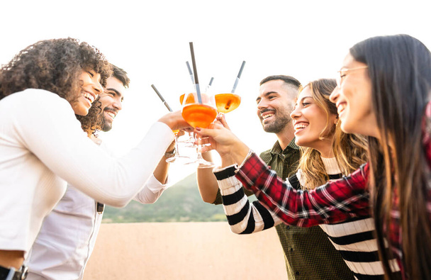 Mixed race happy friends group toasting with spritz glasses outdoor at sunset - Young people having fun together drinking cocktail for aperitif time - Bright vivid filter with focus on bearded men - Фото, изображение